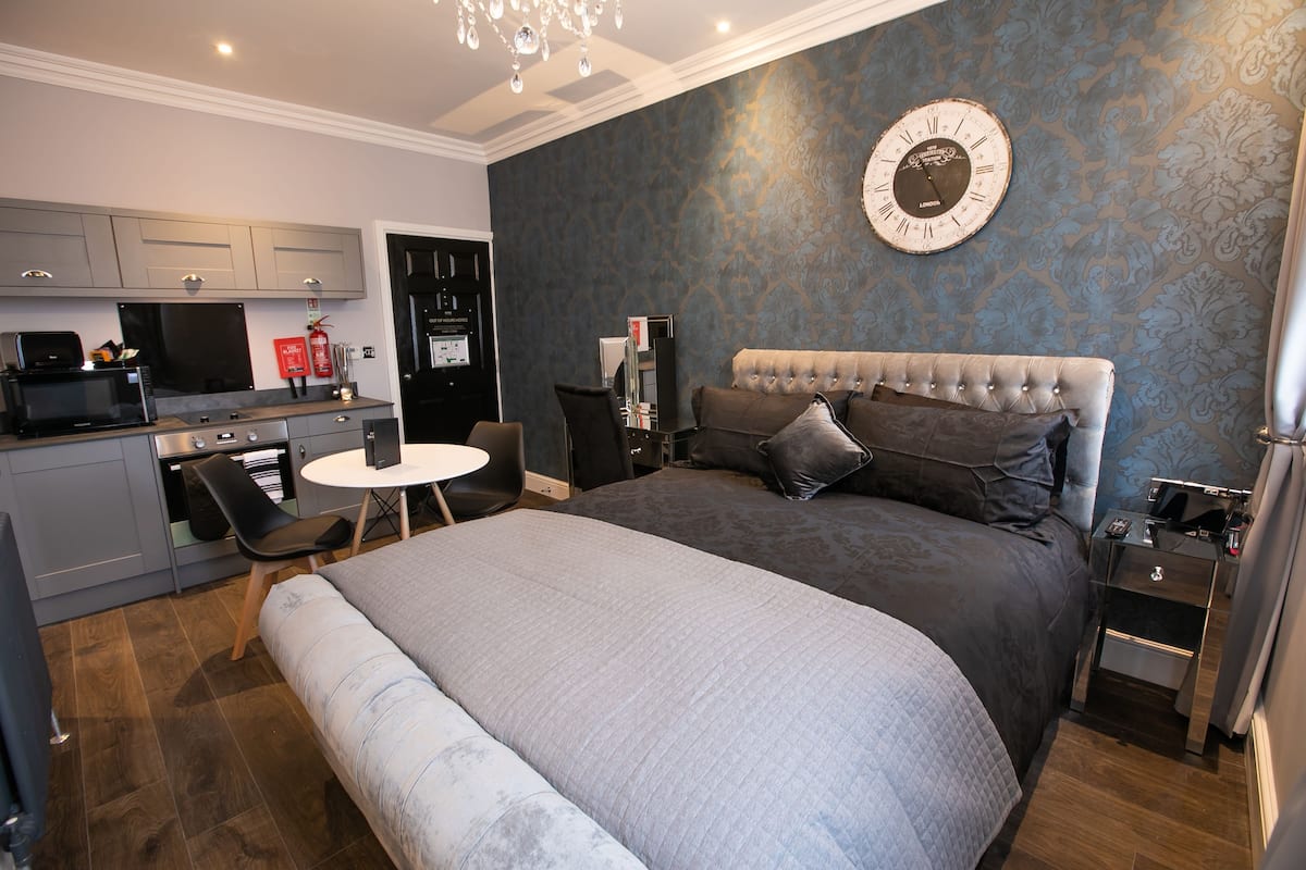 Un dormitorio moderno con una cama grande, un escritorio pequeño y una kitchenette.