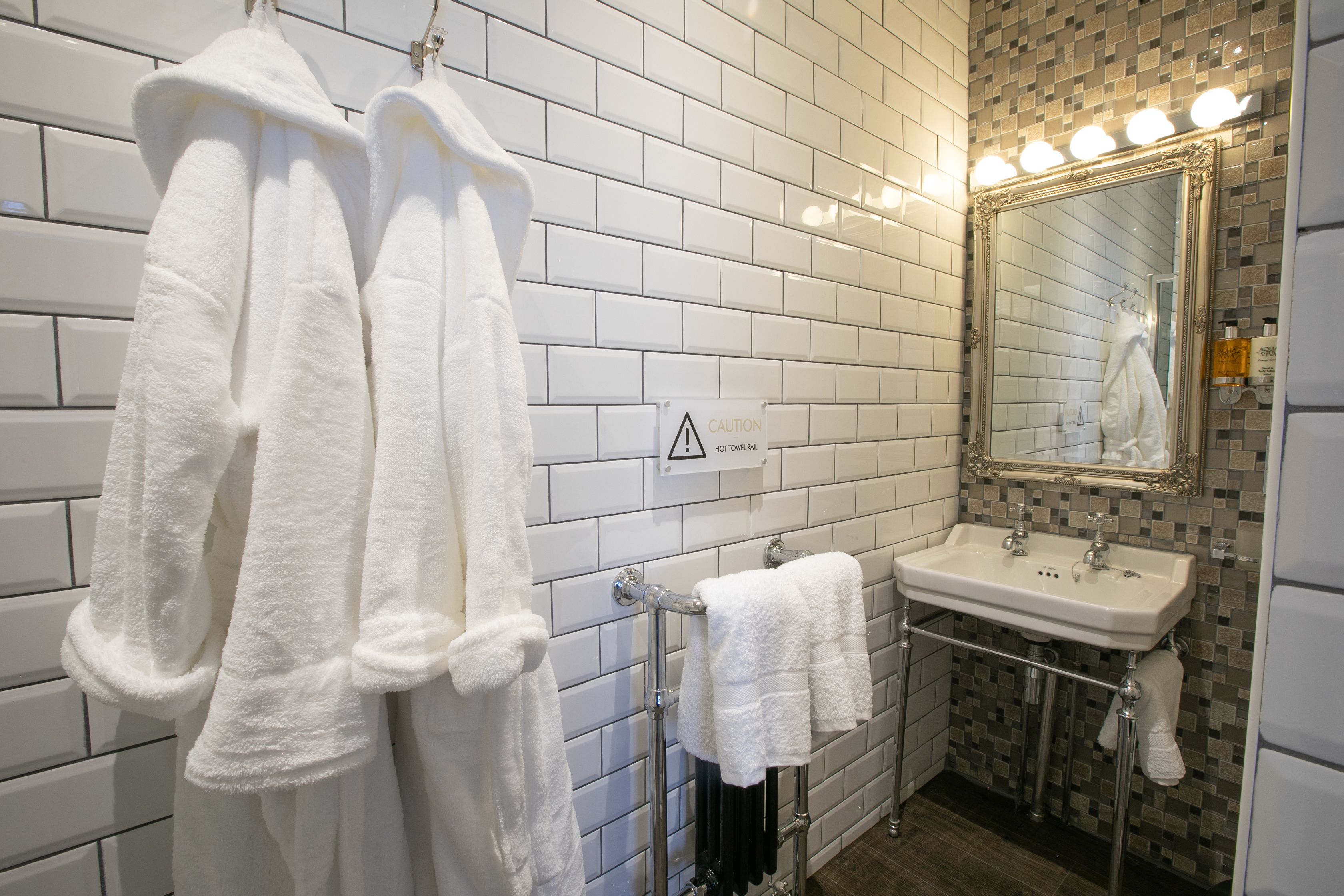 Un baño con paredes de azulejos blancos, un lavabo y un espejo con iluminación.