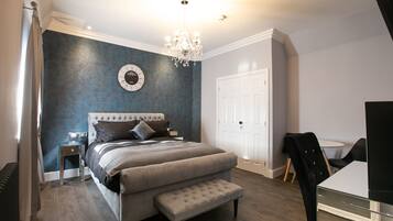 A bedroom with a large bed, a bench, a desk, and a chandelier.