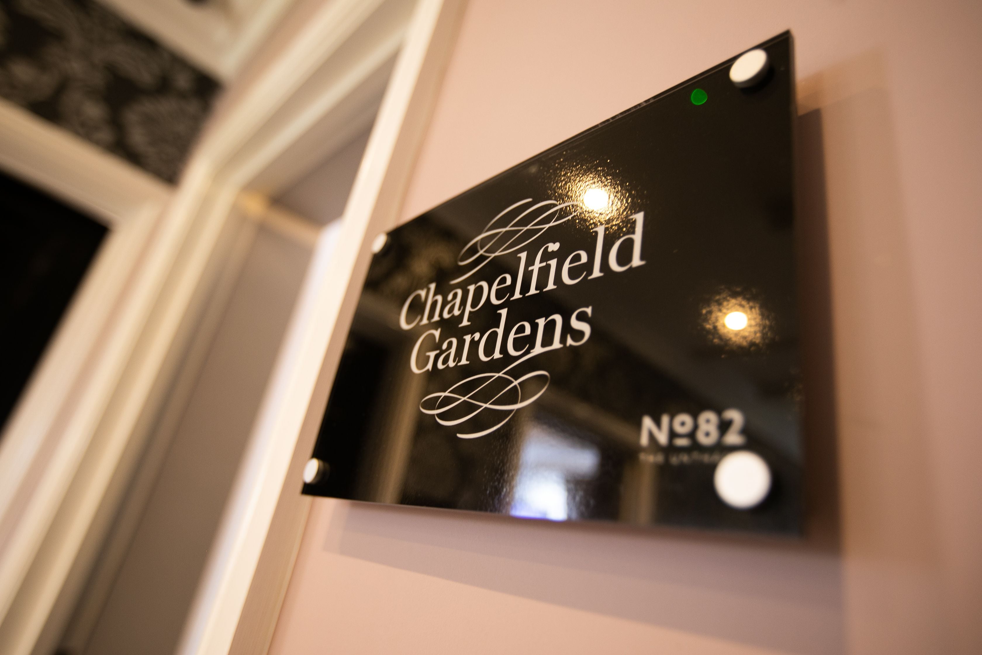 Ein Schild mit dem Text 'Chapelfield Gardens' und 'Nr. 82' an einer Wand.