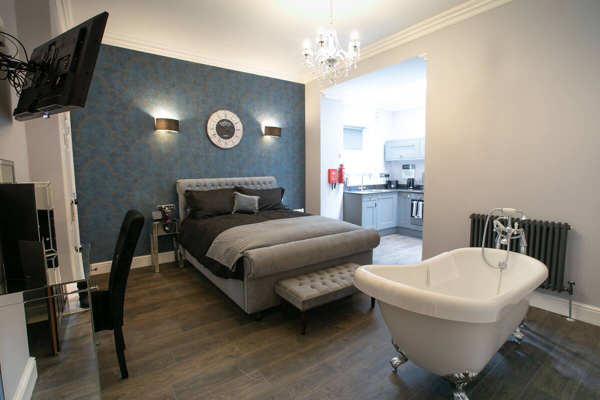 Un dormitorio moderno con una cama grande, un tocador, una bañera y un televisor.