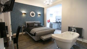 A modern bedroom with a large bed, a vanity, a bathtub, and a television.
