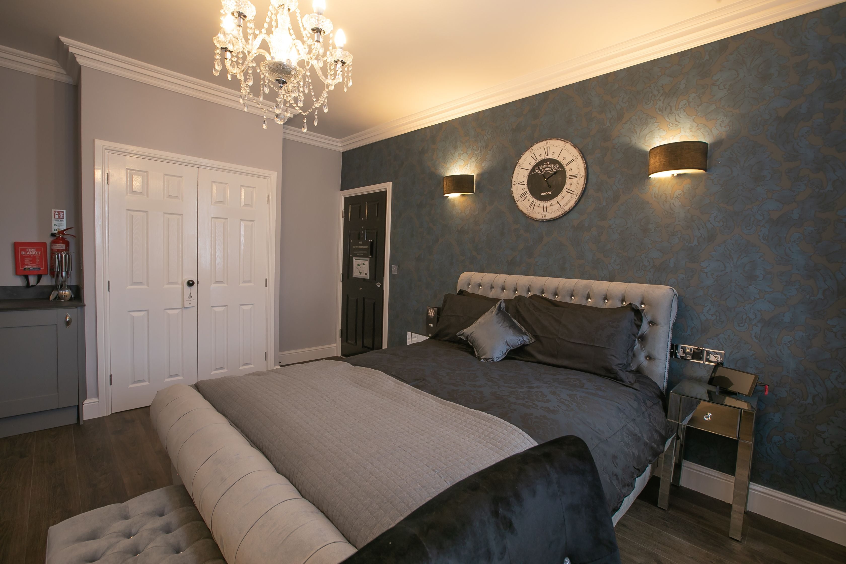 A bedroom with a large bed, a chandelier, a clock, and a nightstand.