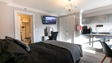 A hotel room with a bed, a TV mounted on the wall, a kitchenette, and a bathroom with a toilet and sink.