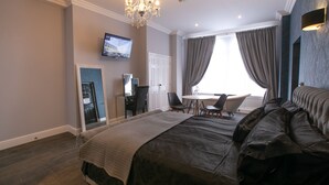 A bedroom with a large bed, a TV mounted on the wall, a chandelier, and a view of the outside through a window. - Number 82 The Unthank (Norwich)