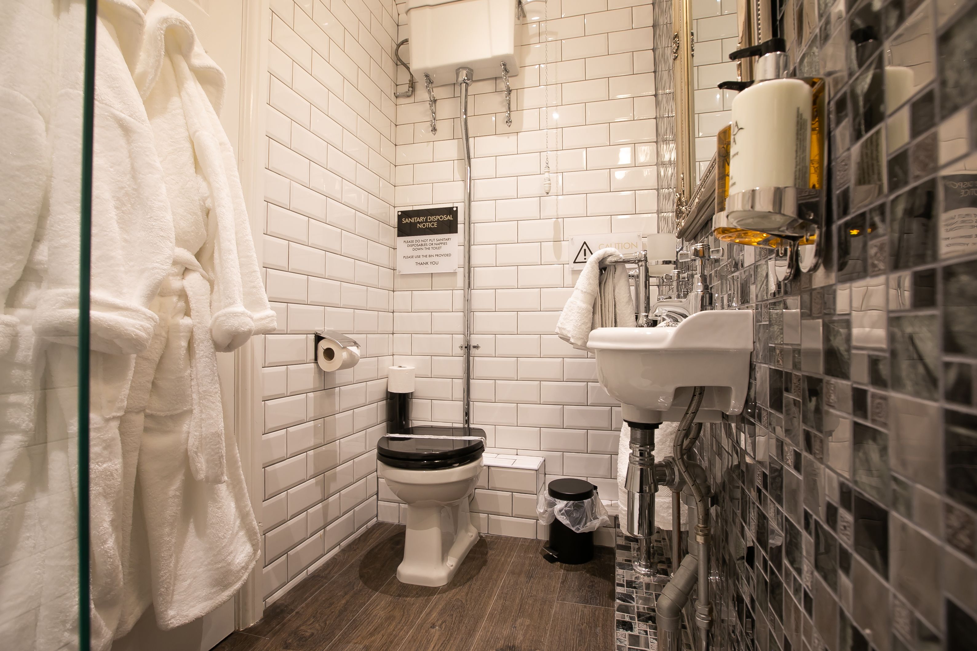 Une salle de bain avec des toilettes, un lavabo et une douche. Des serviettes sont accrochées au mur, et un panneau indique les règles d’hygiène et d’élimination des déchets.