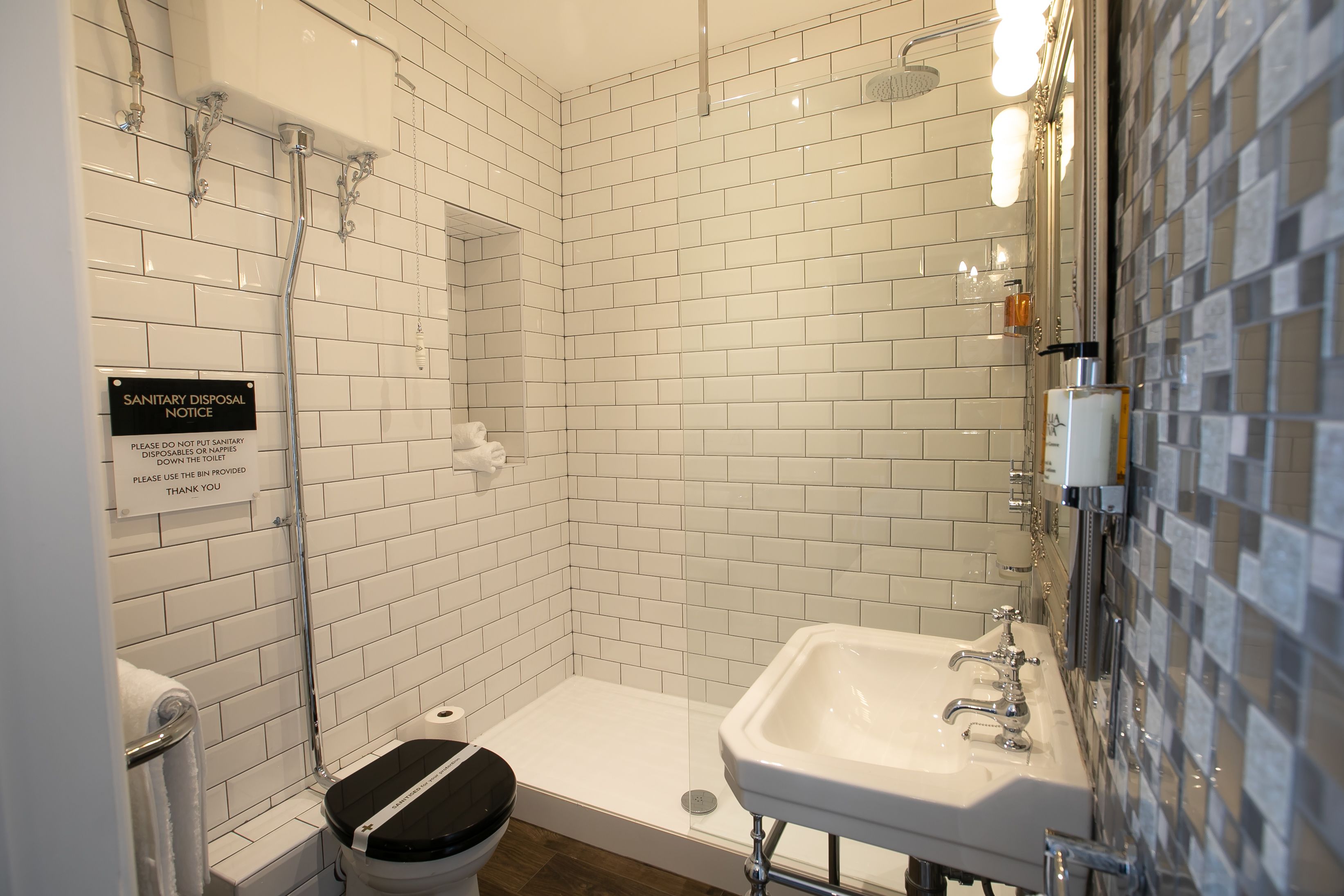 Un baño con azulejos blancos tipo metro, ducha, lavabo e inodoro.