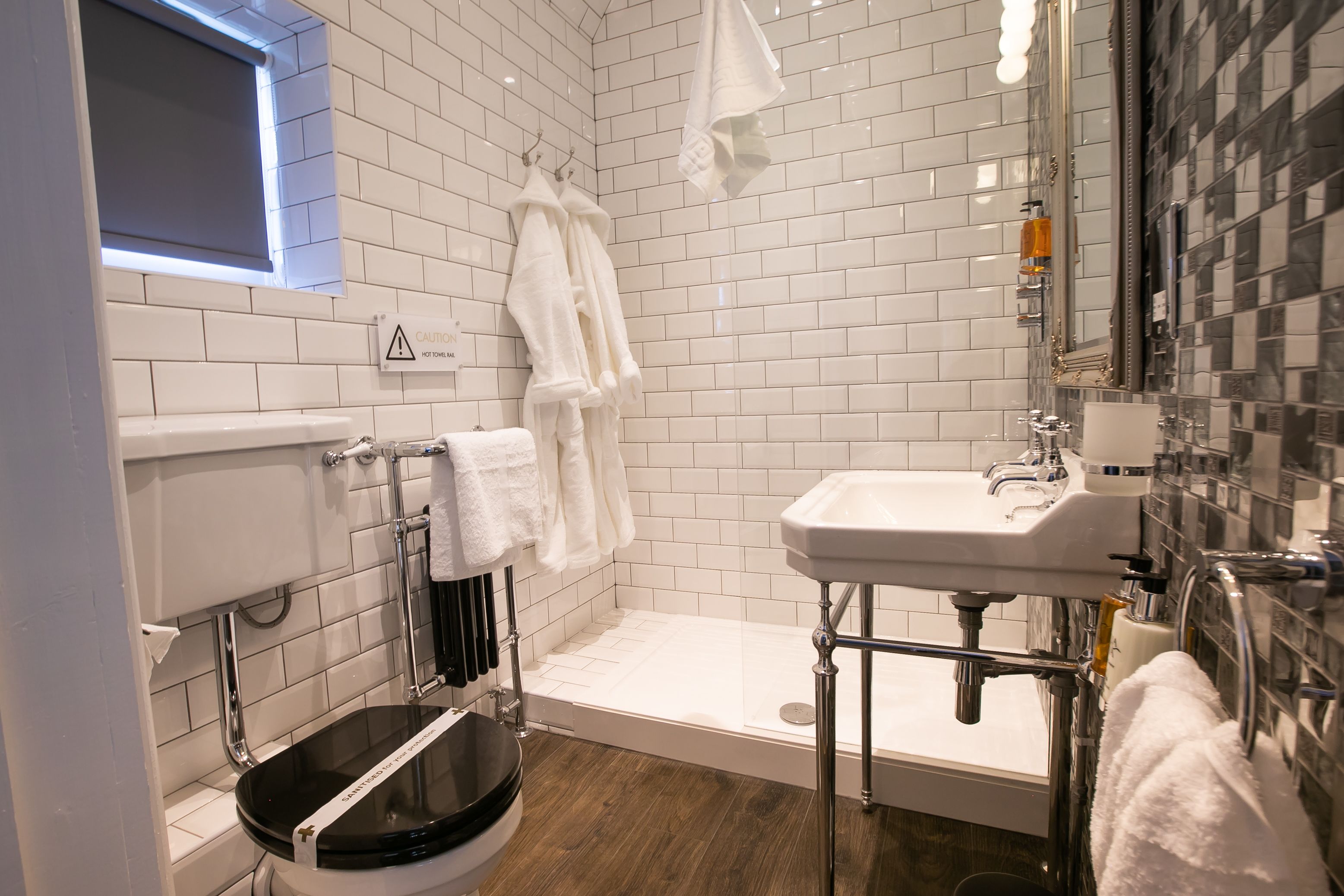 Un baño con inodoro, lavamanos y ducha. Hay toallas blancas colgadas en ganchos.
