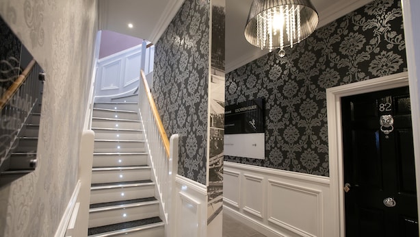 A staircase with white railings and black steps, leading to a room with a black door and a location guide sign. - Number 82 The Unthank (Norwich)