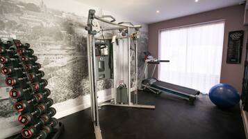 A gym with a wall-mounted dumbbell rack, a weight machine, a treadmill, and a blue exercise ball.