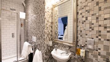 A bathroom with a glass-enclosed shower, a white sink, and a tiled wall with a mosaic pattern.