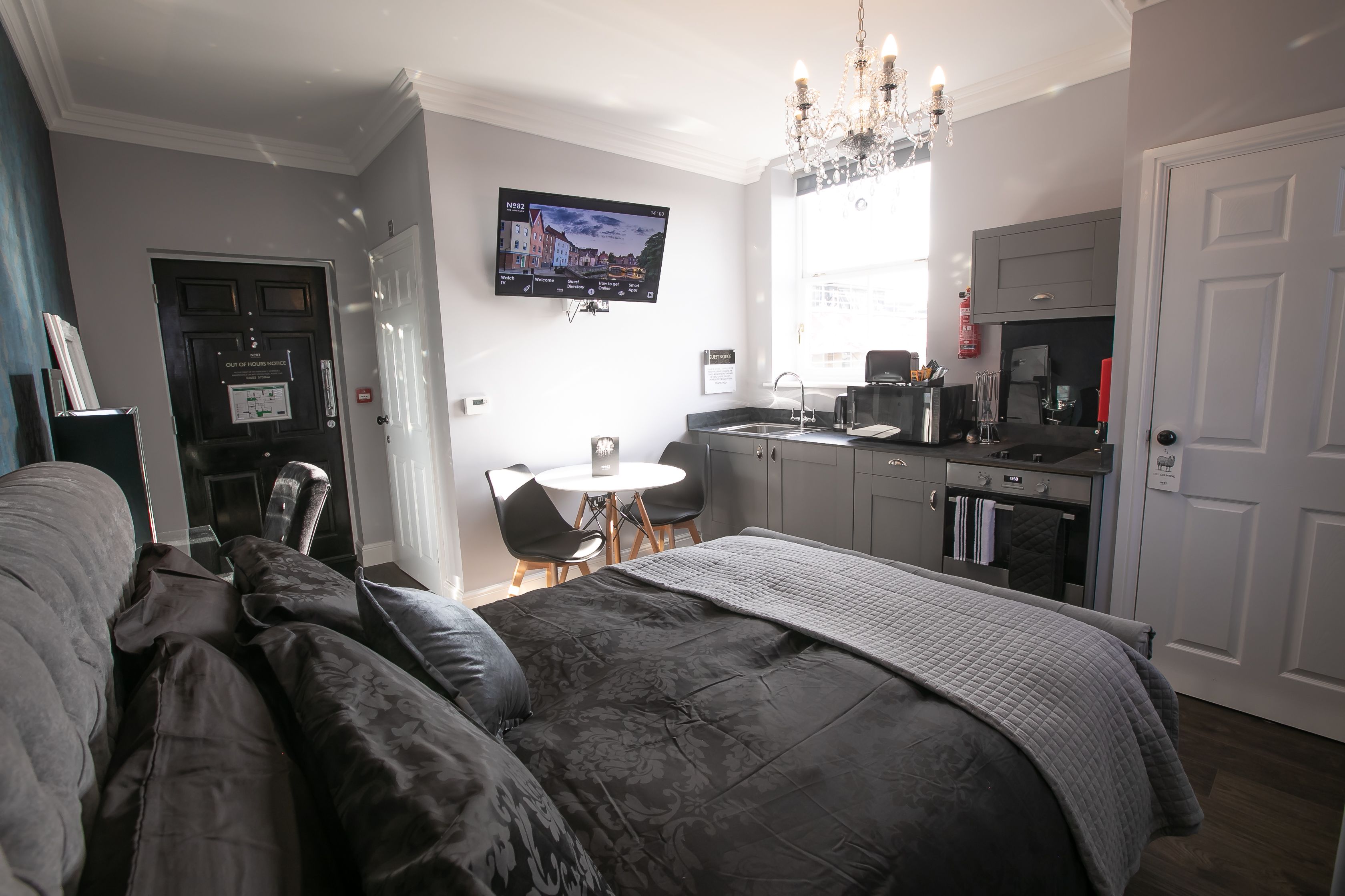 Ein modernes Hotelzimmer mit Bett, Essbereich, Küche und einem an der Wand befestigten Fernseher.