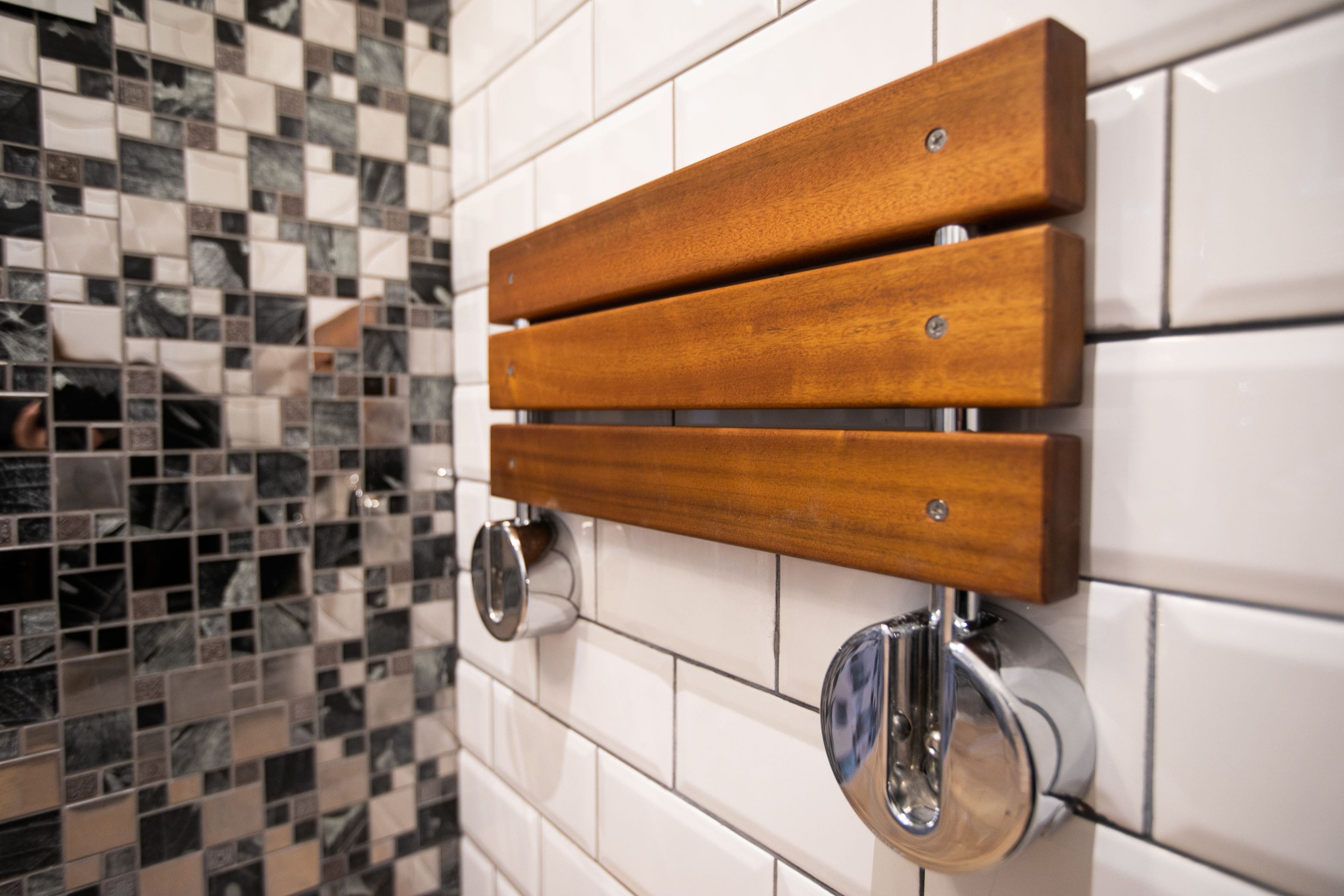 Une salle de bain avec un banc en bois fixé au mur, un miroir et un sol carrelé.