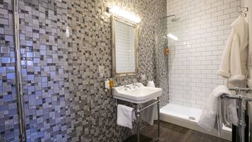 A modern bathroom with a mosaic tile wall, a white sink, a large mirror, and a bathtub.