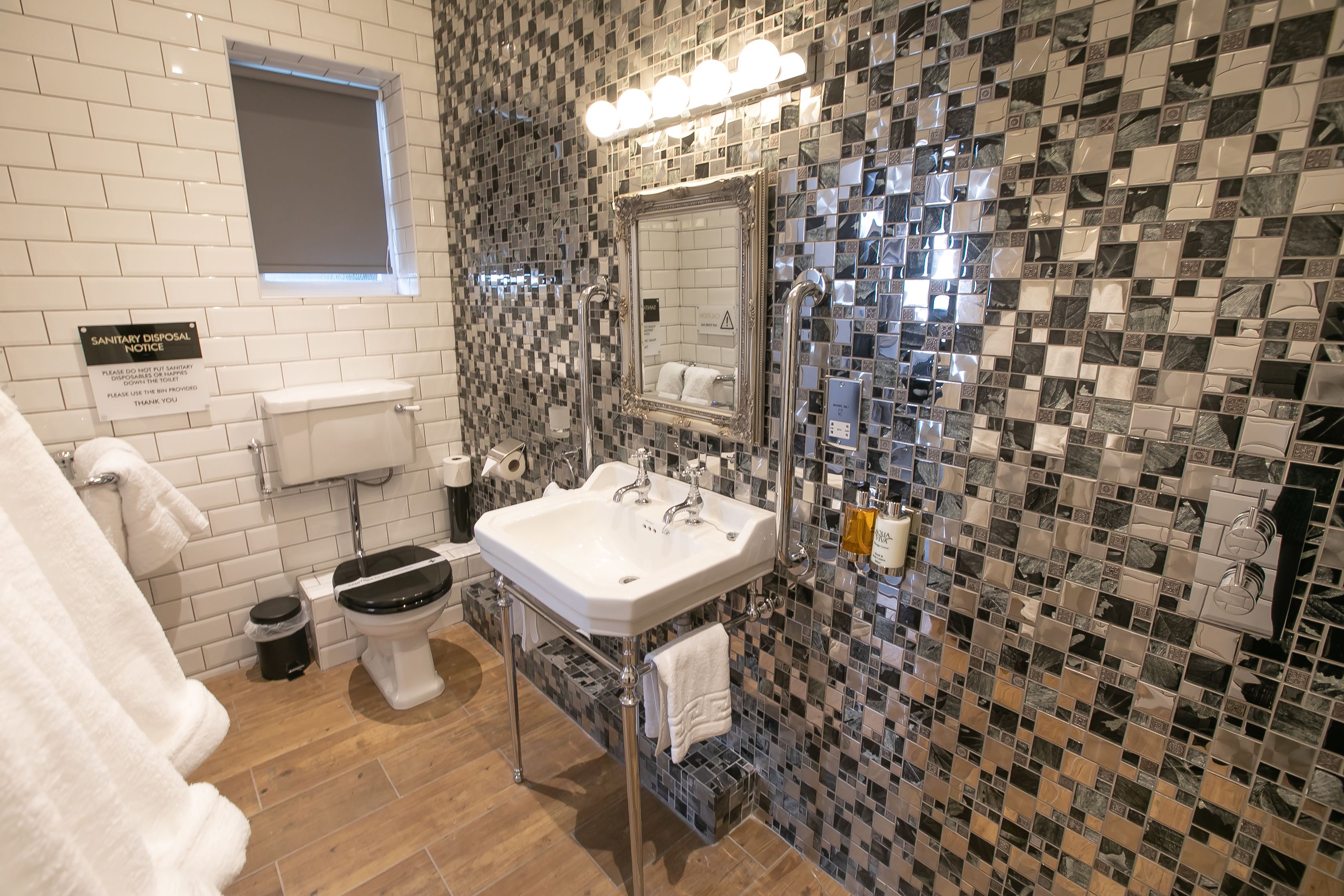 A bathroom with a white toilet, a sink with a mirror, and a tiled wall with a checkered pattern.