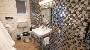 Une salle de bain avec des toilettes blanches, un lavabo avec un miroir et un mur carrelé à motifs à carreaux.
