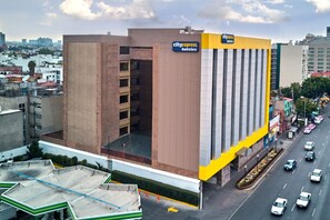 Un bâtiment de l’hôtel CityExpress, doté d’une architecture moderne, se distingue par sa façade jaune et blanche bien visible, et dispose d’un parking où l’on peut voir des voitures.
