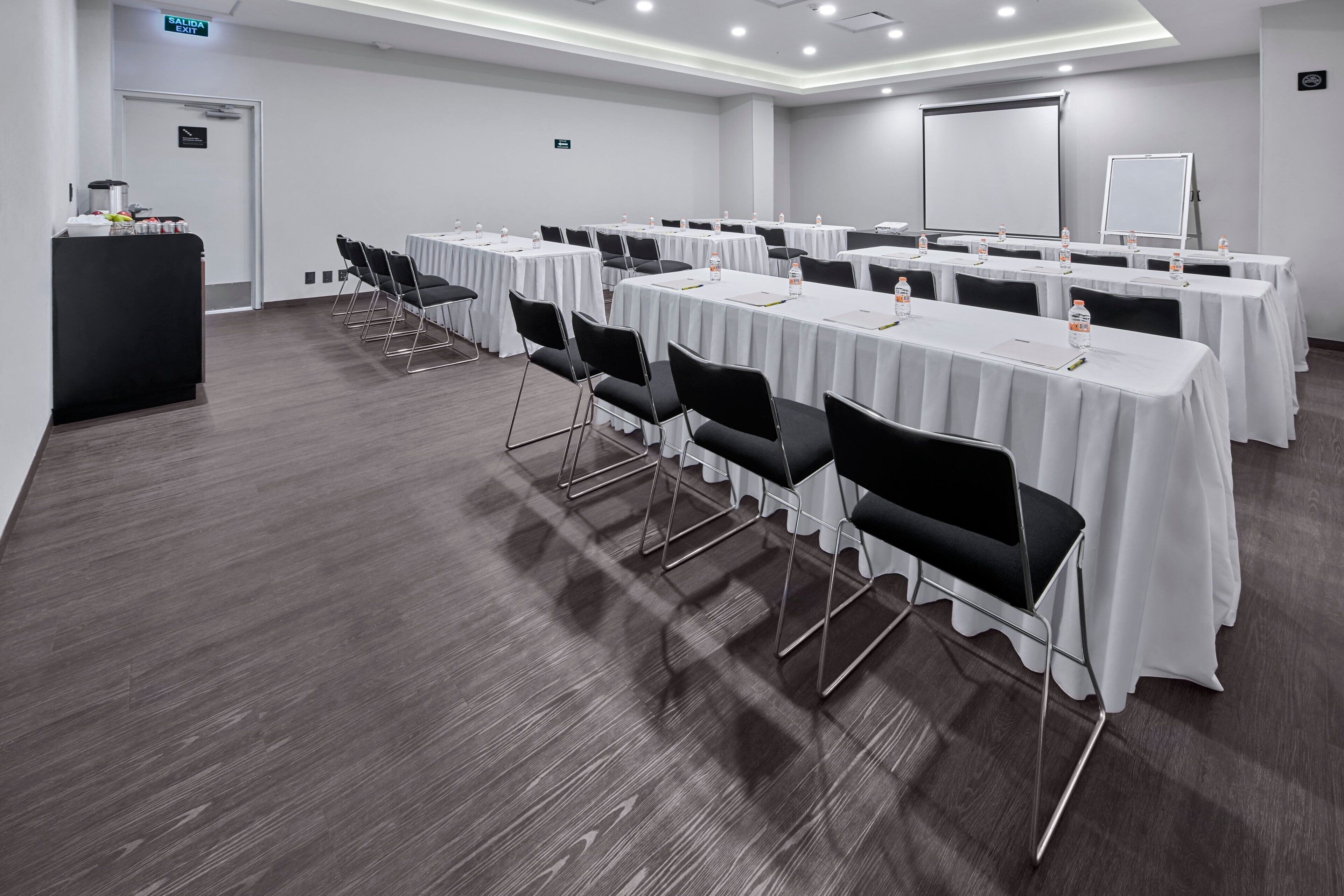 Une salle de conférence équipée de plusieurs tables et chaises, d’un pupitre et d’un écran de projection.