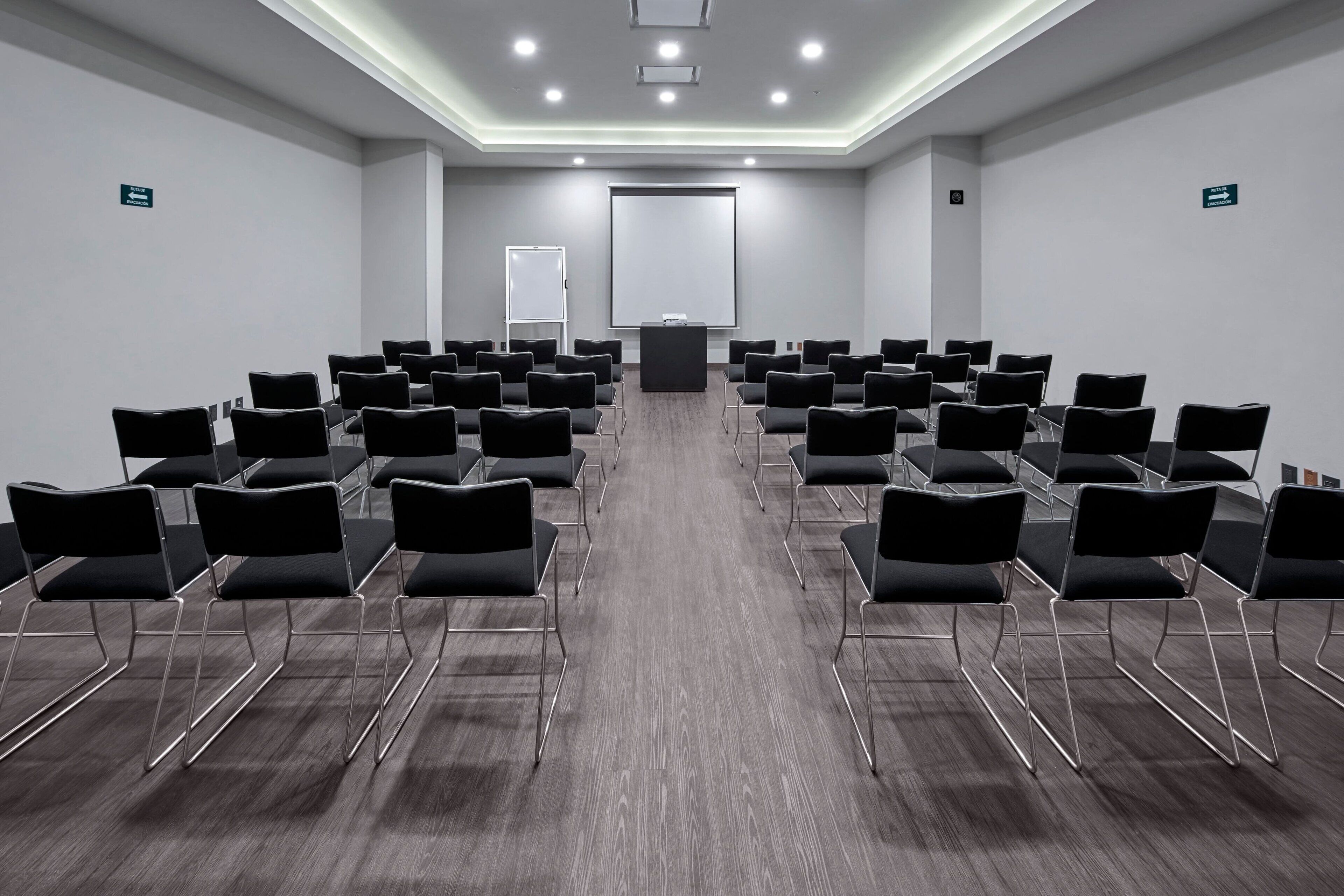 A conference room with rows of black chairs, a podium, and a projector screen.