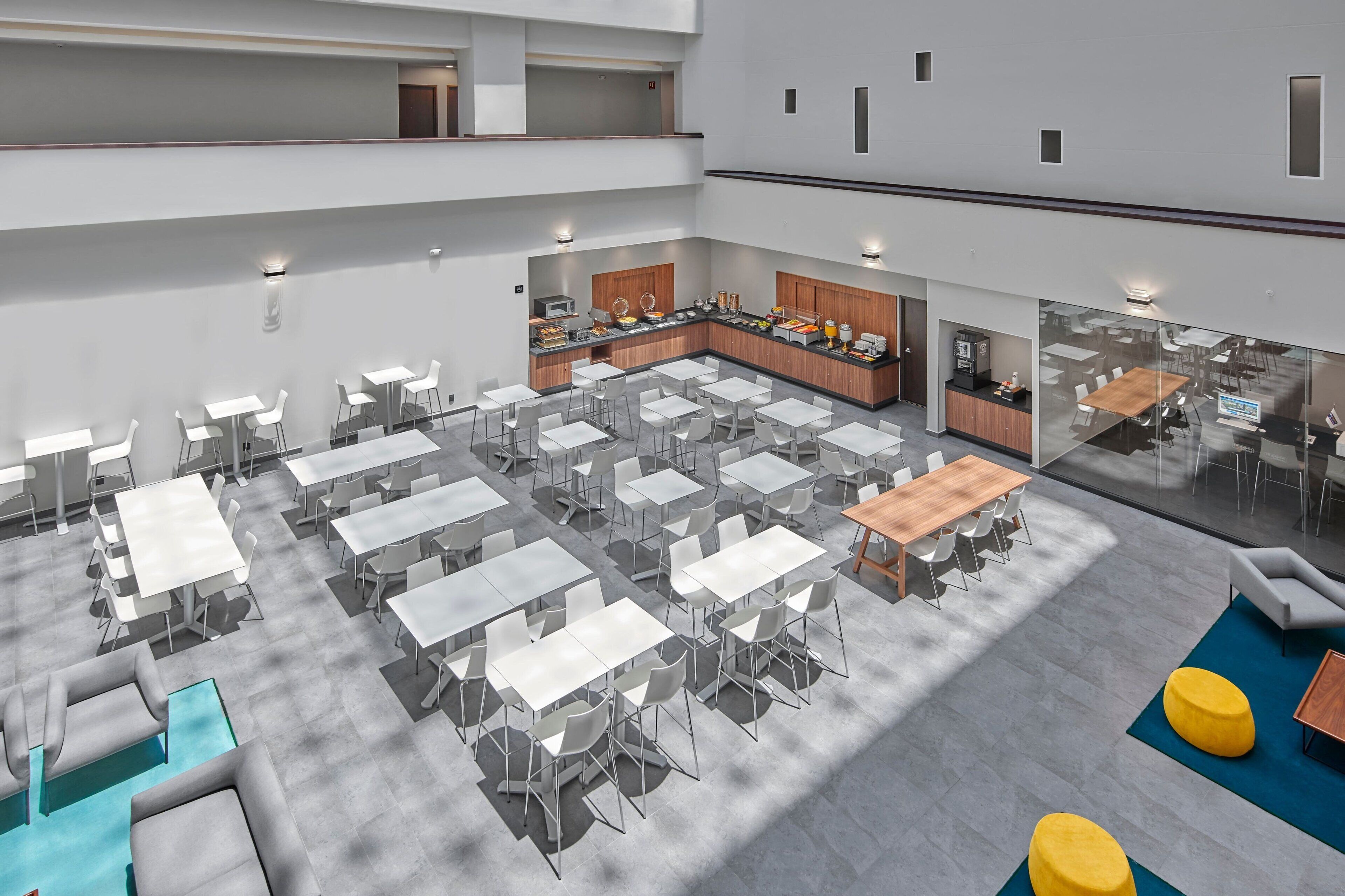 A spacious indoor area with multiple tables and chairs, a kitchen area, and a seating area with sofas and ottomans.