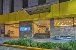 Entrada de un hotel con el letrero de City Express, una escalera que lleva al lobby y un toldo amarillo.