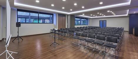 A conference room with rows of chairs, a projector stand, and large windows with city views.