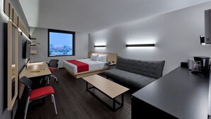 A modern hotel room with a bed, sofa, desk, chairs, and a coffee machine.