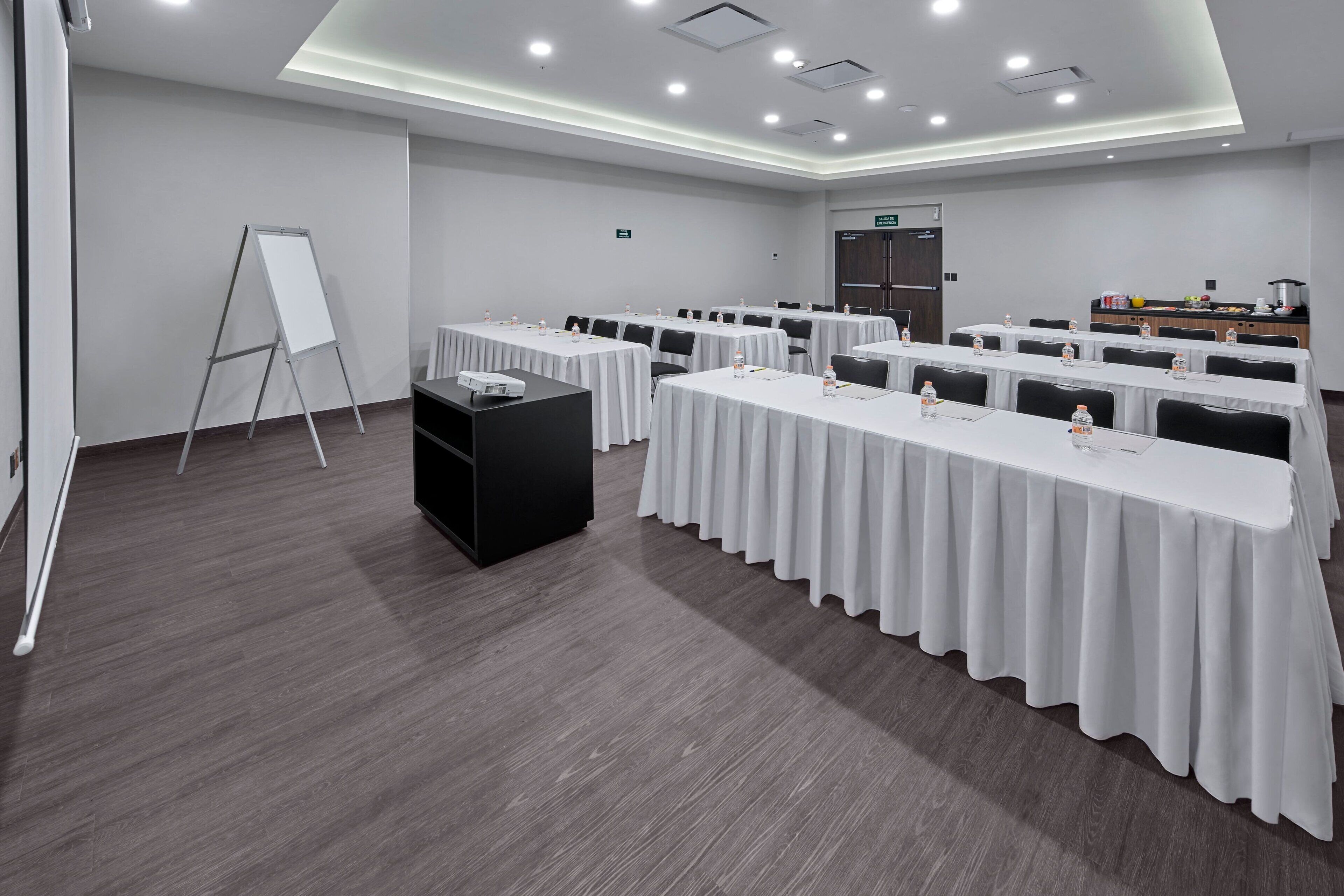 Un salón de conferencias con varias mesas, una pizarra y una zona de kitchenette.