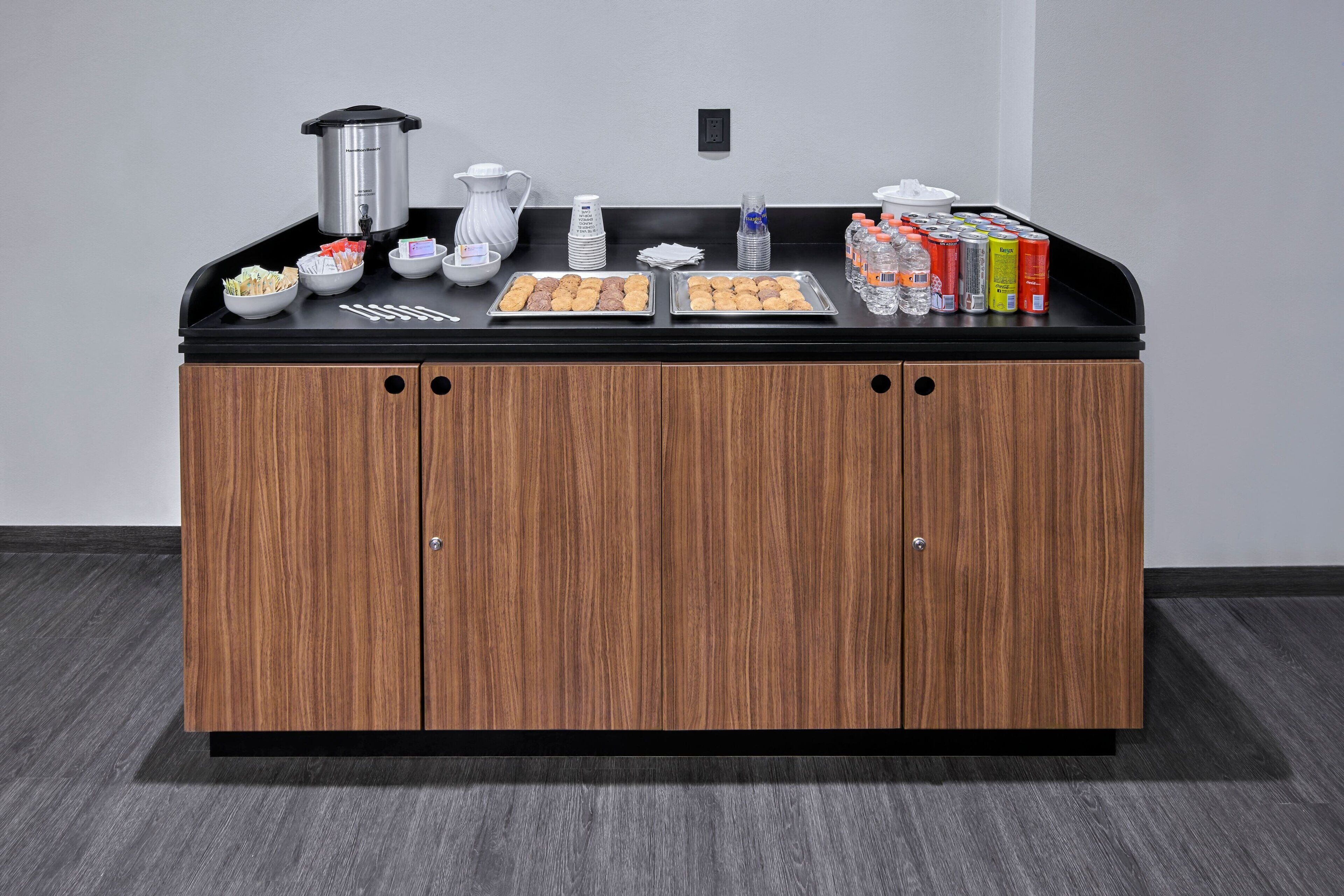 A kitchenette with a coffee maker, tea kettle, and trays of food.