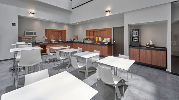 A modern kitchen with white tables and chairs, a microwave, and a coffee machine.