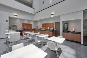 Une cuisine moderne avec des tables et des chaises blanches, un four à micro-ondes et une machine à café.