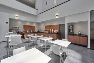Una cocina moderna con mesas y sillas blancas, un microondas y una cafetera.