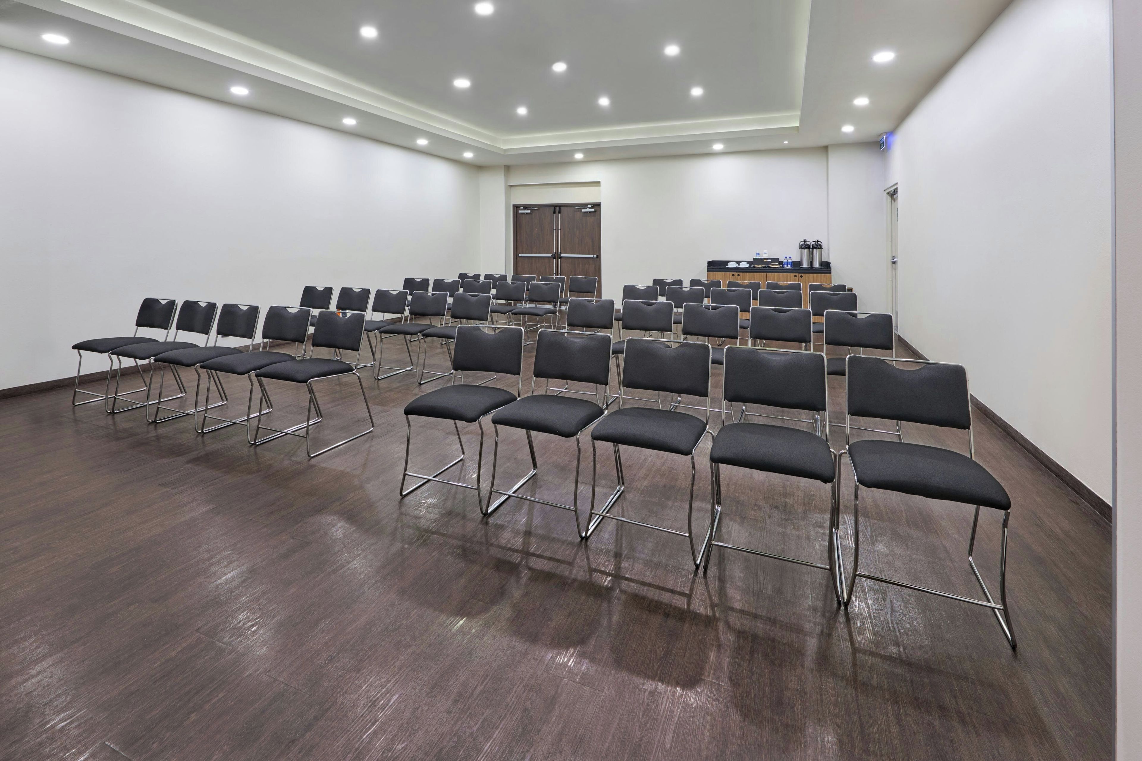 Konferenssihuone, jossa on riveissä tuoleja, puhujapönttö ja ovi.