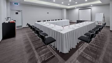 Ein Konferenzraum mit einem langen Tisch, Stühlen, einer Projektorleinwand und einer Whiteboard-Tafel.