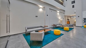 A modern lobby with a grey sofa, a wooden coffee table, and yellow ottomans on a blue rug.