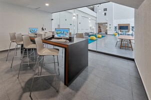 Un espacio de oficina moderno con una zona de escritorio central, múltiples monitores de ordenador y una piscina visible a través de paredes de cristal.