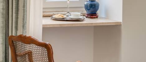 A room with a wooden chair with a purple cushion, a small table with a blue vase and a white cup, and a window with curtains.