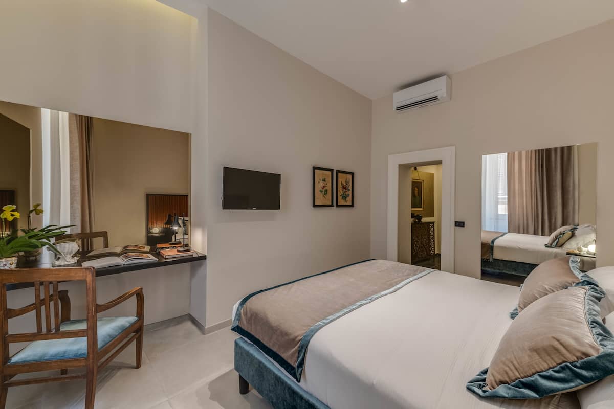 A modern hotel room with a large bed, a desk with a chair, a flat-screen TV, and a large mirror.