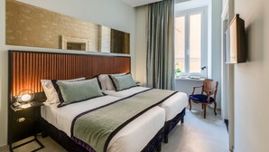 A hotel room with two beds, a nightstand with a lamp, a chair, a large window with curtains, and a flat-screen TV mounted on the wall. - Adrianus Hotel (Rome)