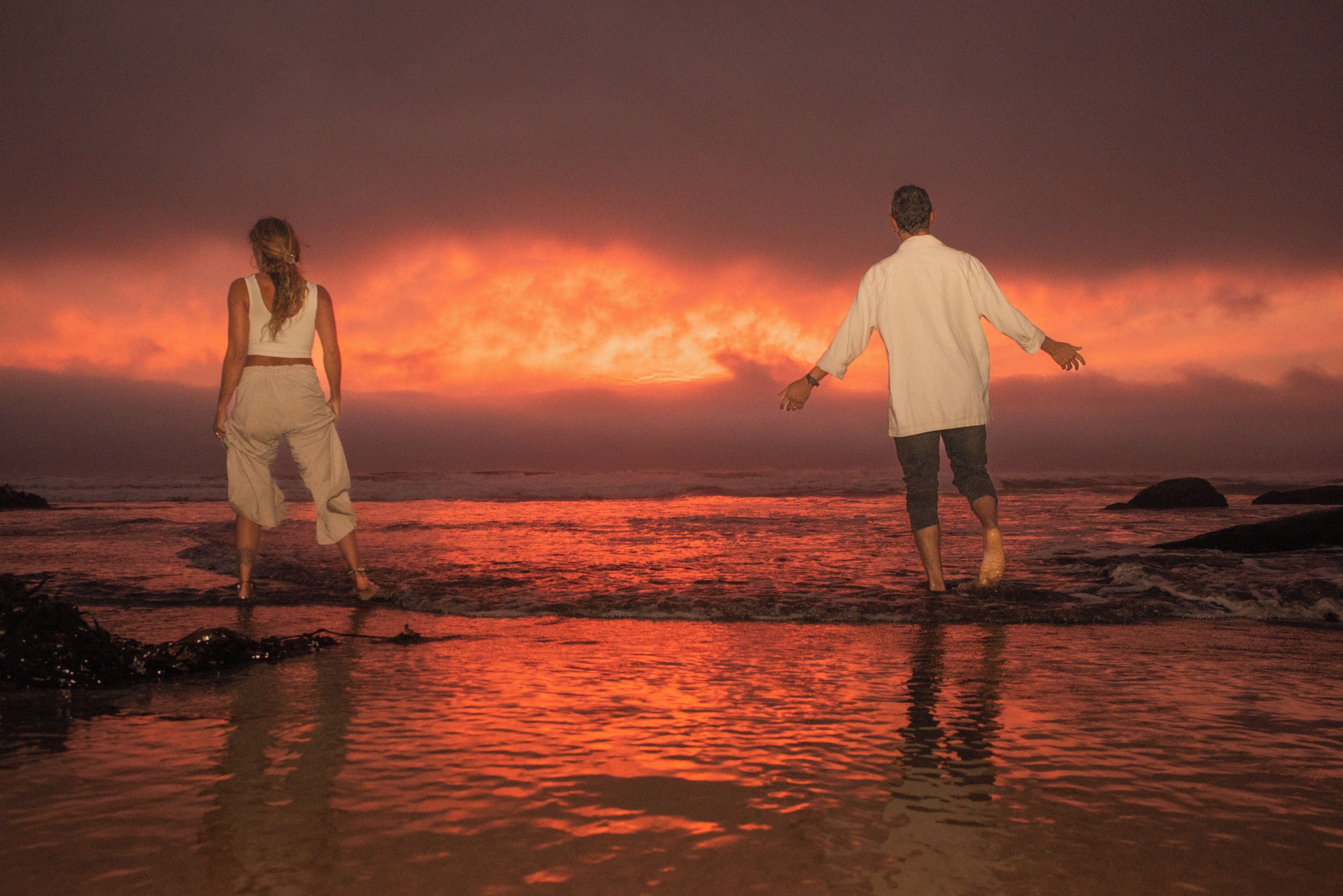 Two people walking on a beach at sunset.