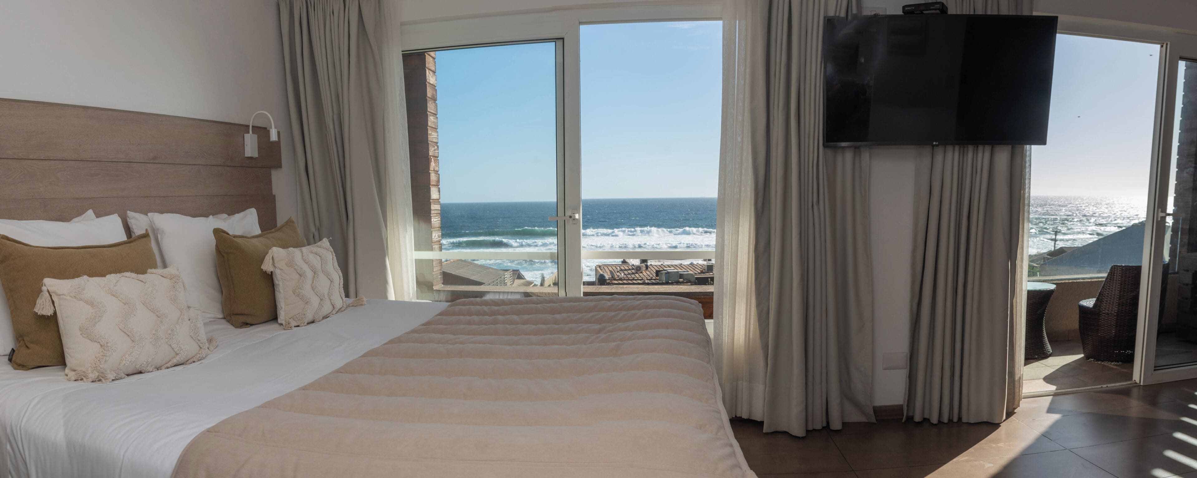 A bedroom with a large bed, a TV, and a view of the ocean.