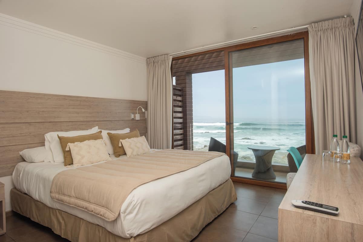 Habitación de hotel con una cama grande, un escritorio con control remoto y vista al océano.
