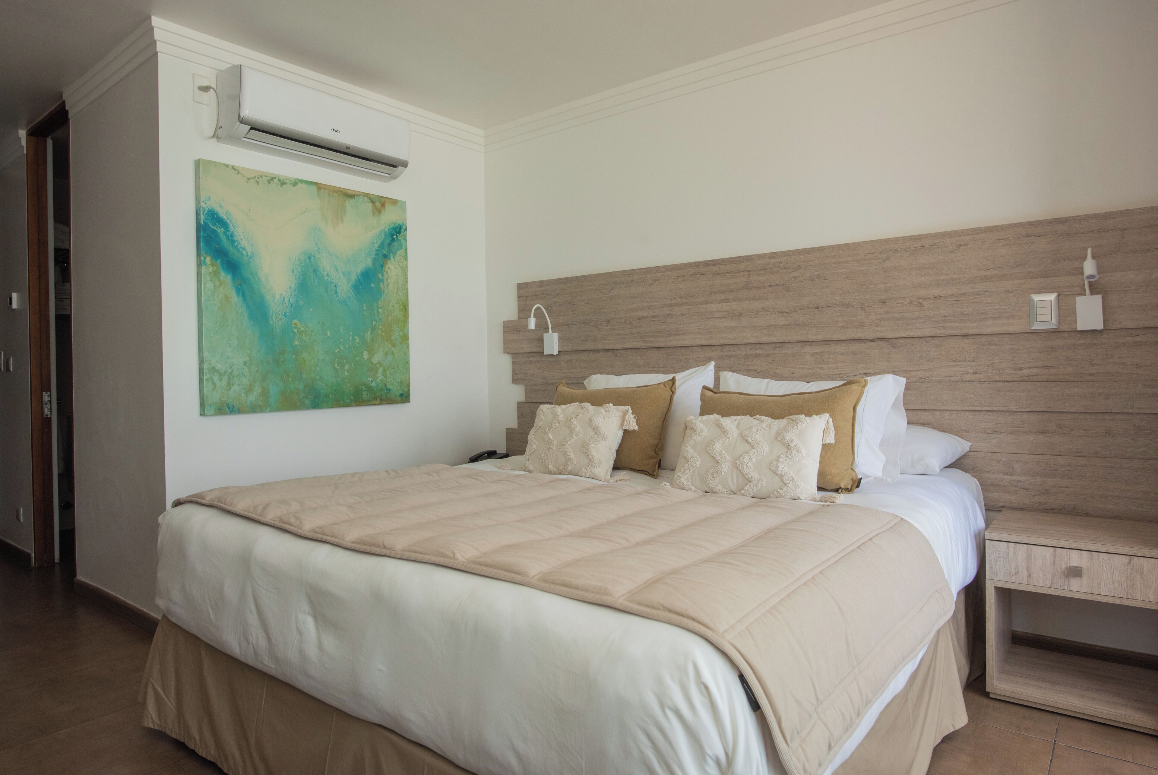 Une chambre d’hôtel avec un lit, un climatiseur fixé au mur, un tableau et une table de chevet.