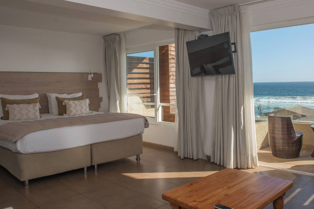 Un dormitorio con cama, televisor, balcón con vista al mar y una mesa de madera.