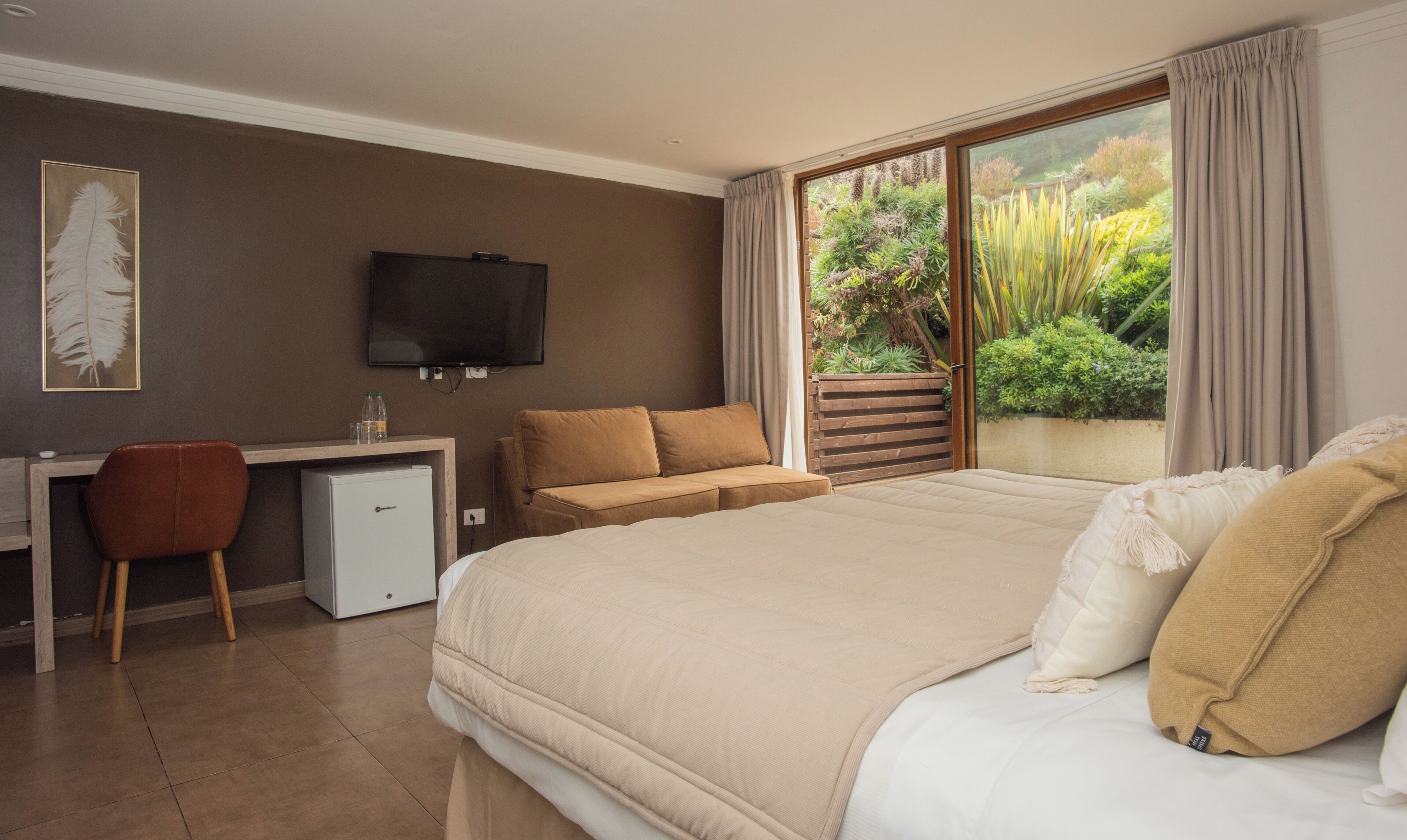 Ein Schlafzimmer mit Bett, Schreibtisch, Fernseher und Blick ins Grüne.
