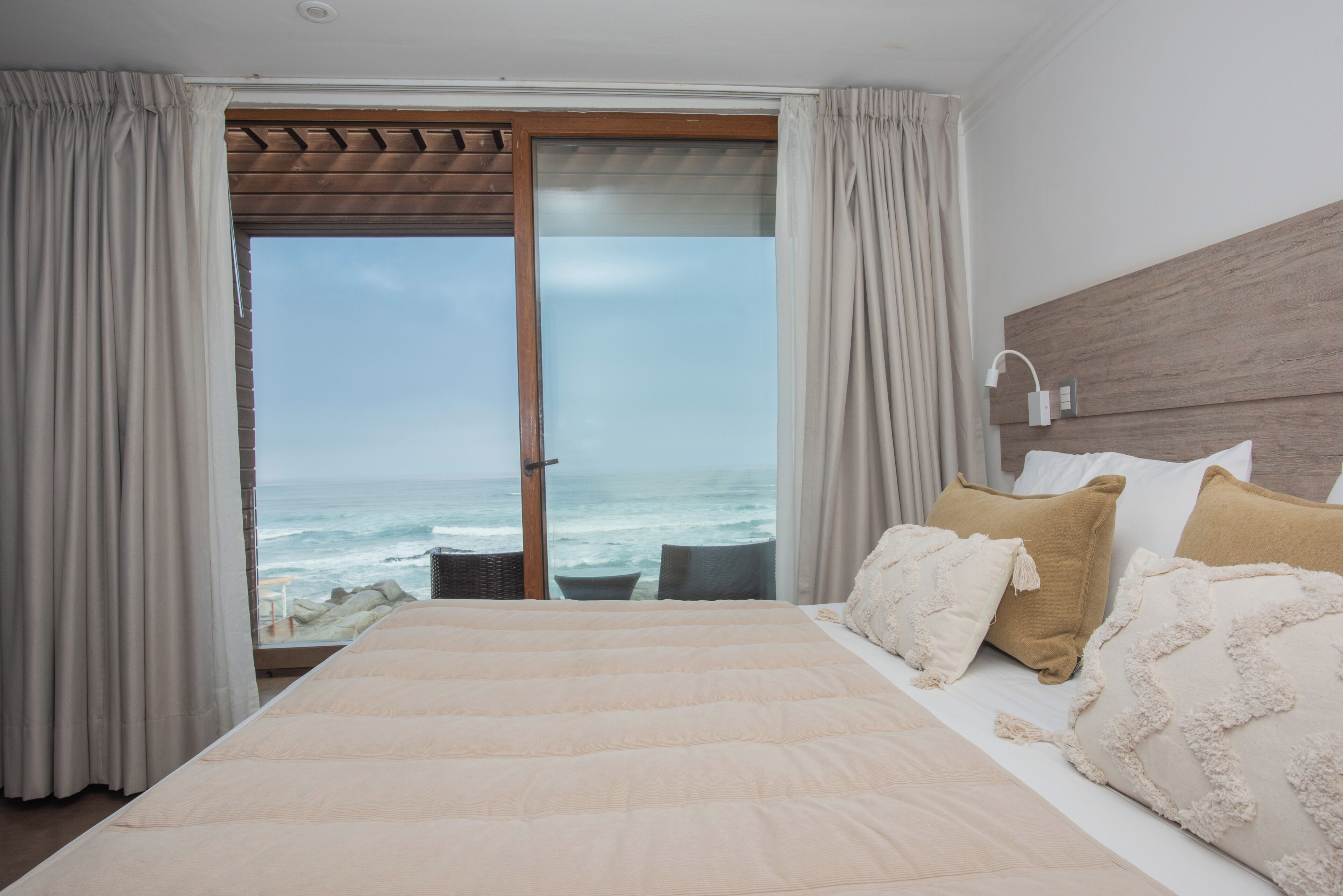 A bedroom with a large bed, a wooden headboard, a view of the ocean, and a sliding glass door.