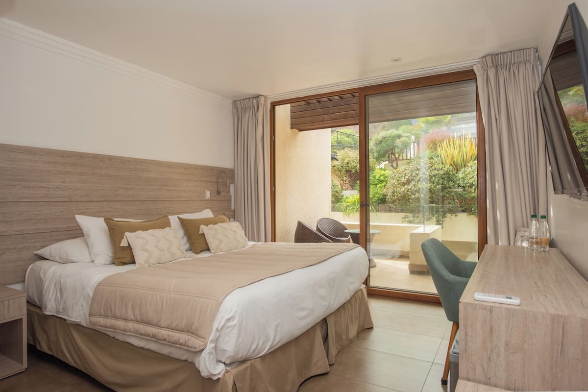 Habitación de hotel con una cama, un escritorio, una silla y un ventanal corredero que da a un balcón.