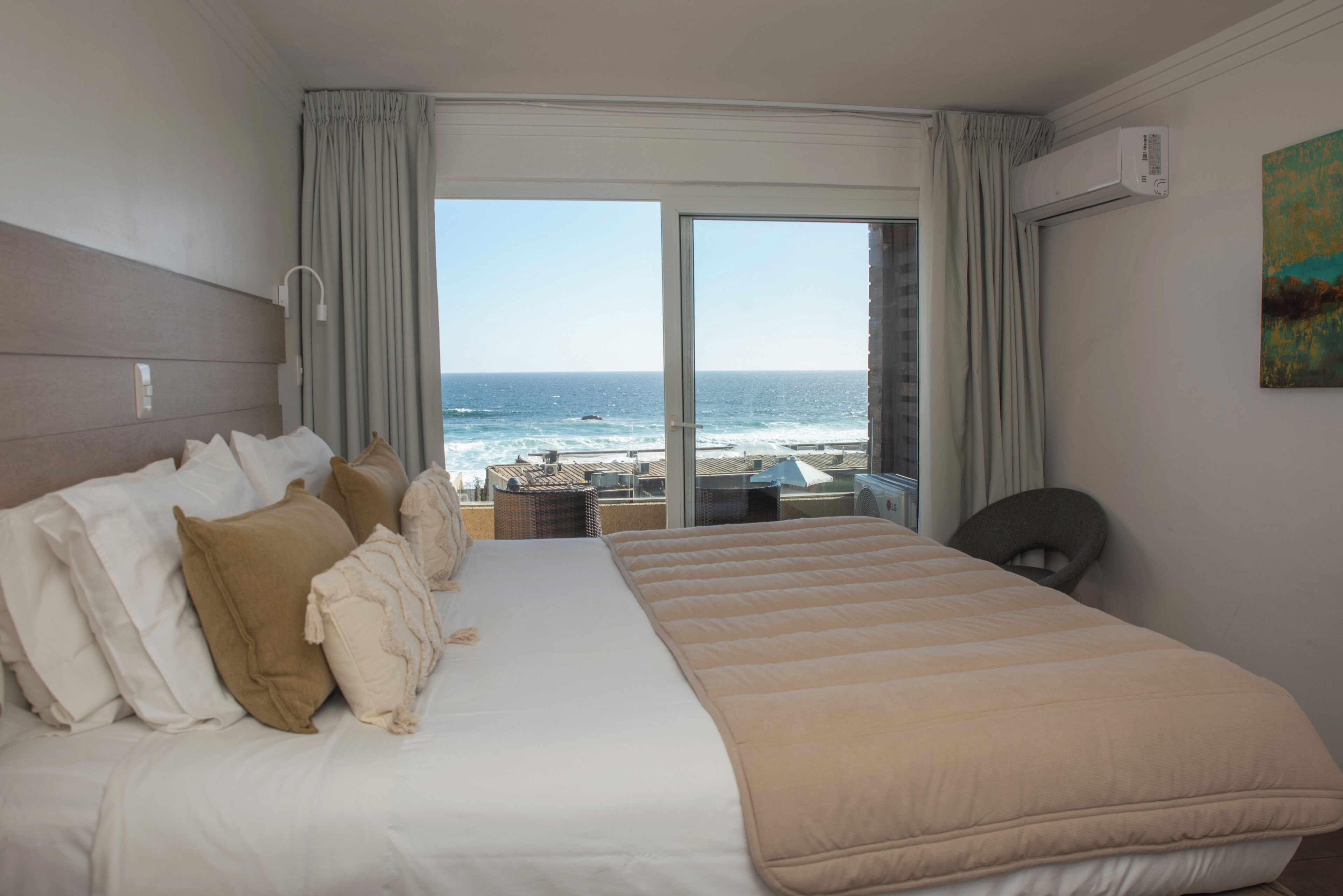 Habitaci ón de hotel con una cama grande, vista al océano, un balcón con mesa y sillas, y un equipo de aire acondicionado en la pared.