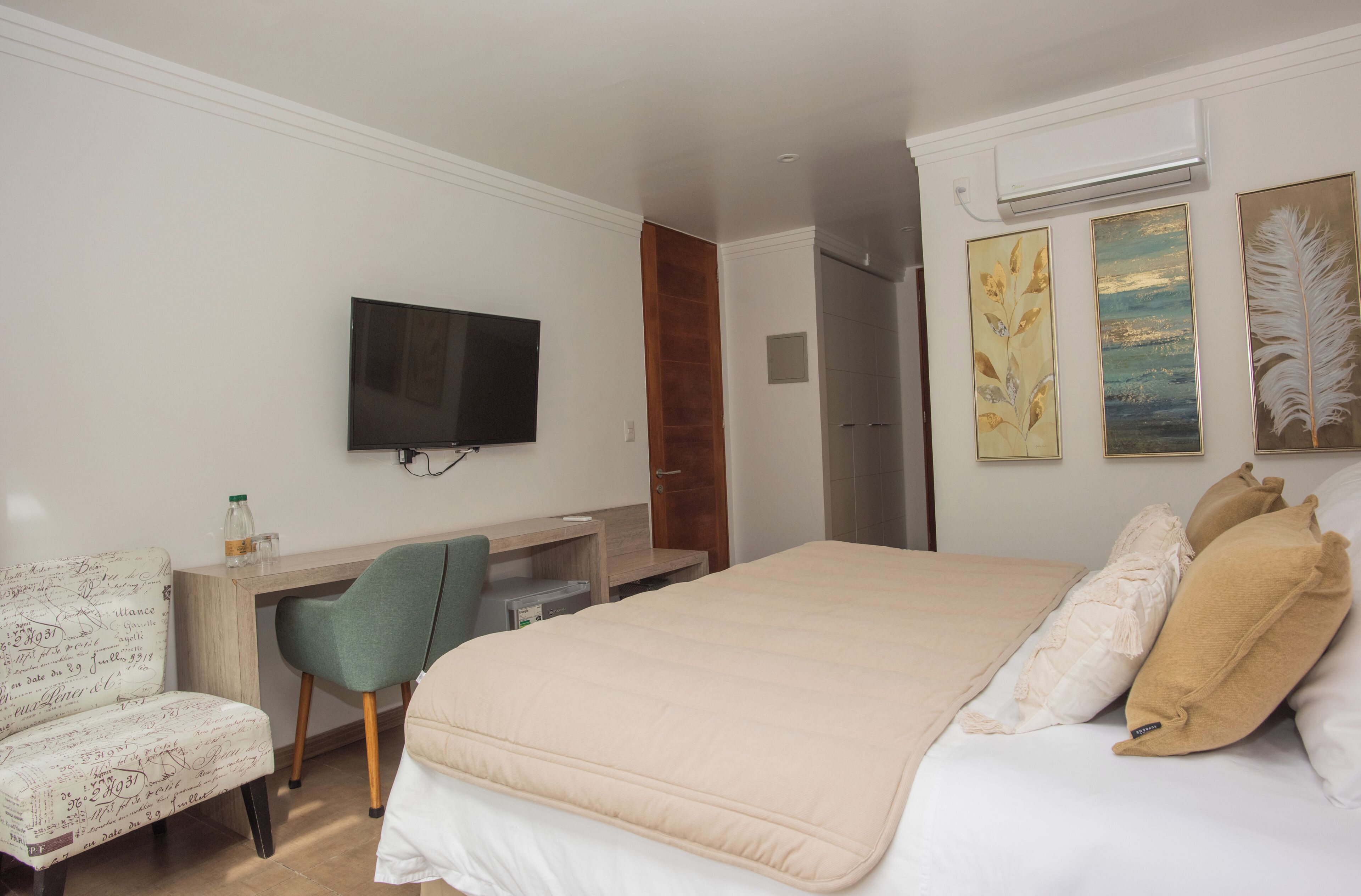 A hotel room with a bed, a desk, a chair, a television, and artwork on the wall.