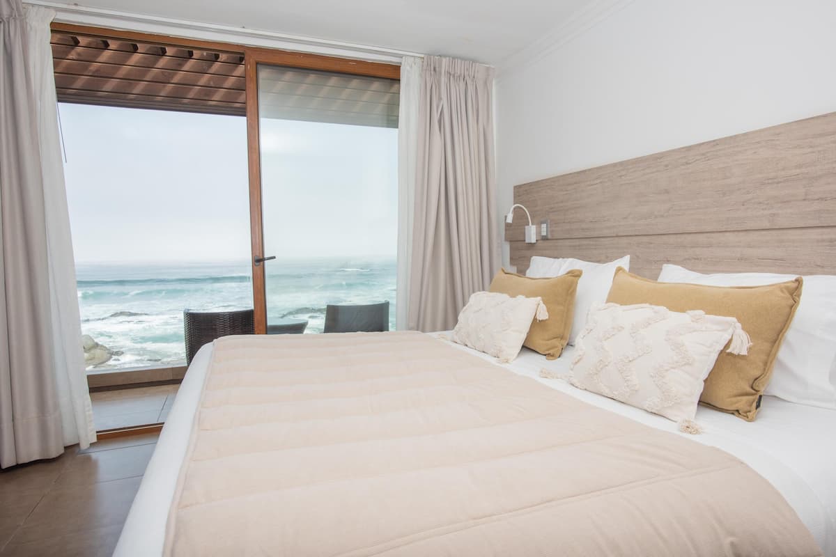Un dormitorio con una cama grande, cabecera de madera, vista al océano y balcón con cortinas.